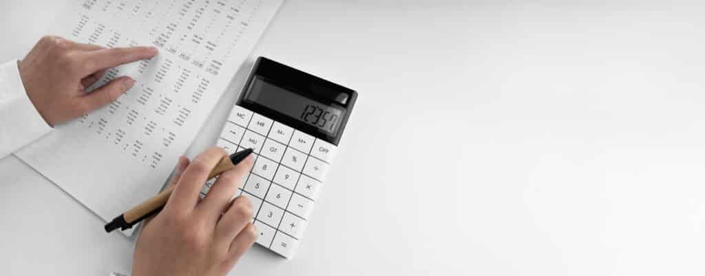 Human hands with a calculator and a pen on top of financial documents.