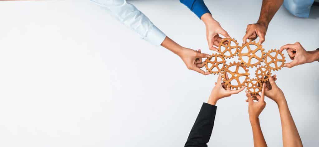A group of people holds wooden gears, symbolizing teamwork and cooperation.